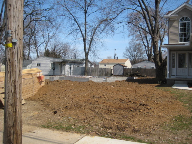 The same site before the build: an empty graded lot with lumber delivered