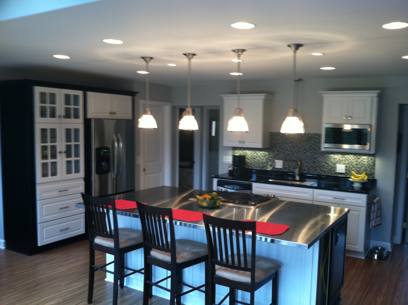 Remodeled kitchen with white cabinets, pendant lights and a stainless island